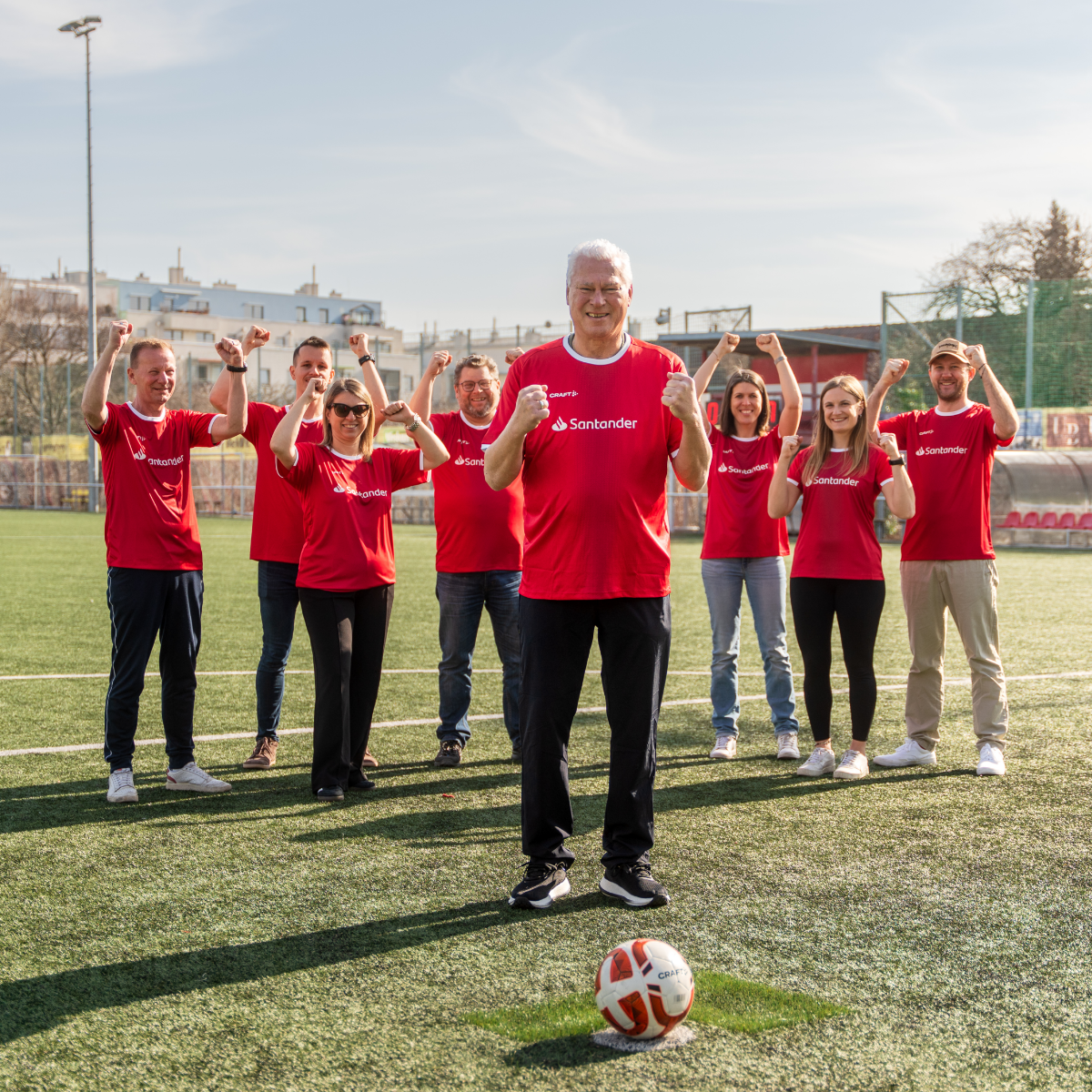 Toni Polster steht vor Santander-Mitarbeitern im roten Fußball-Trikot.