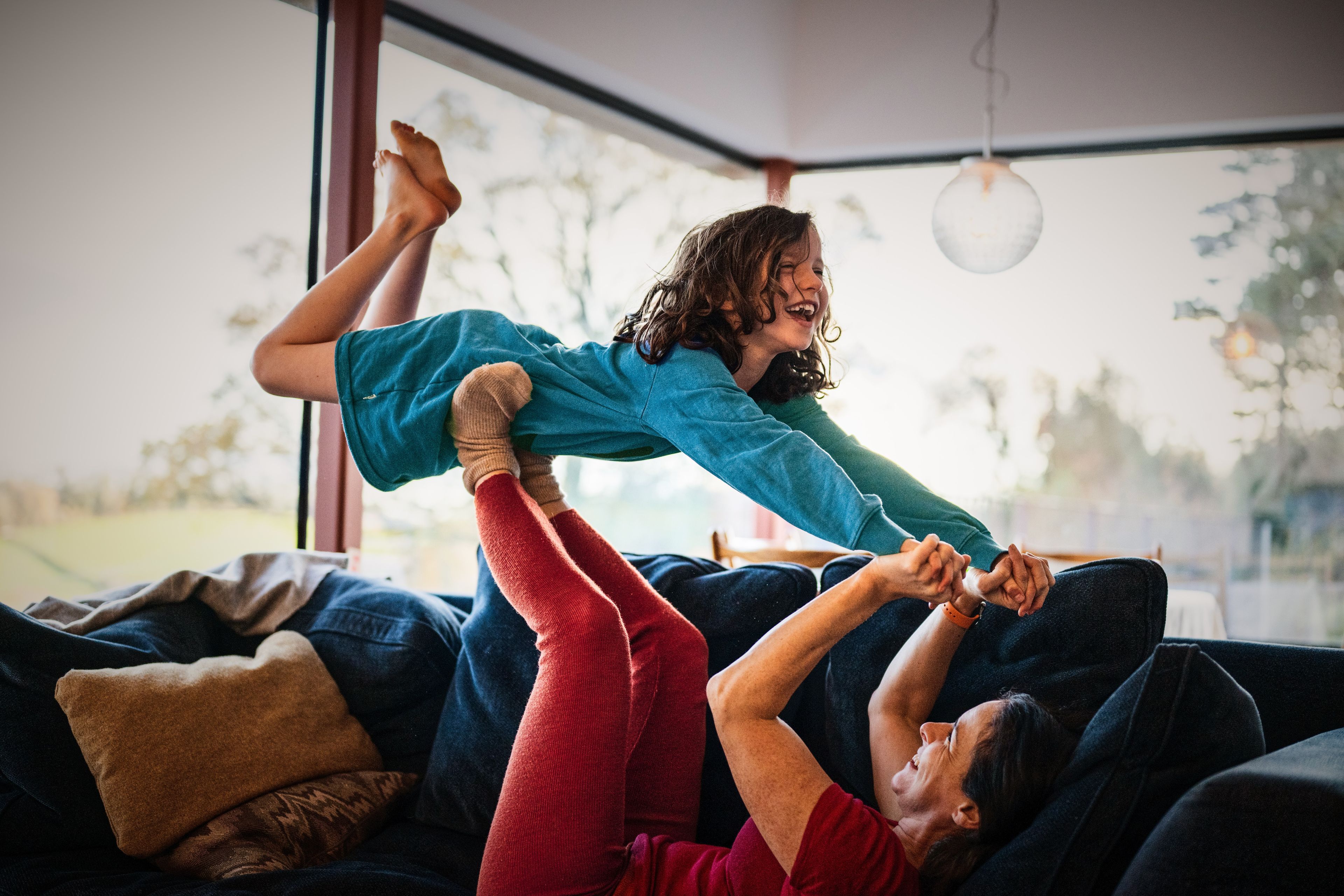 Ein kleines Mädchen lacht vor Freude, während ihre Mutter sie beim Spielen auf dem Sofa in die Luft hebt.