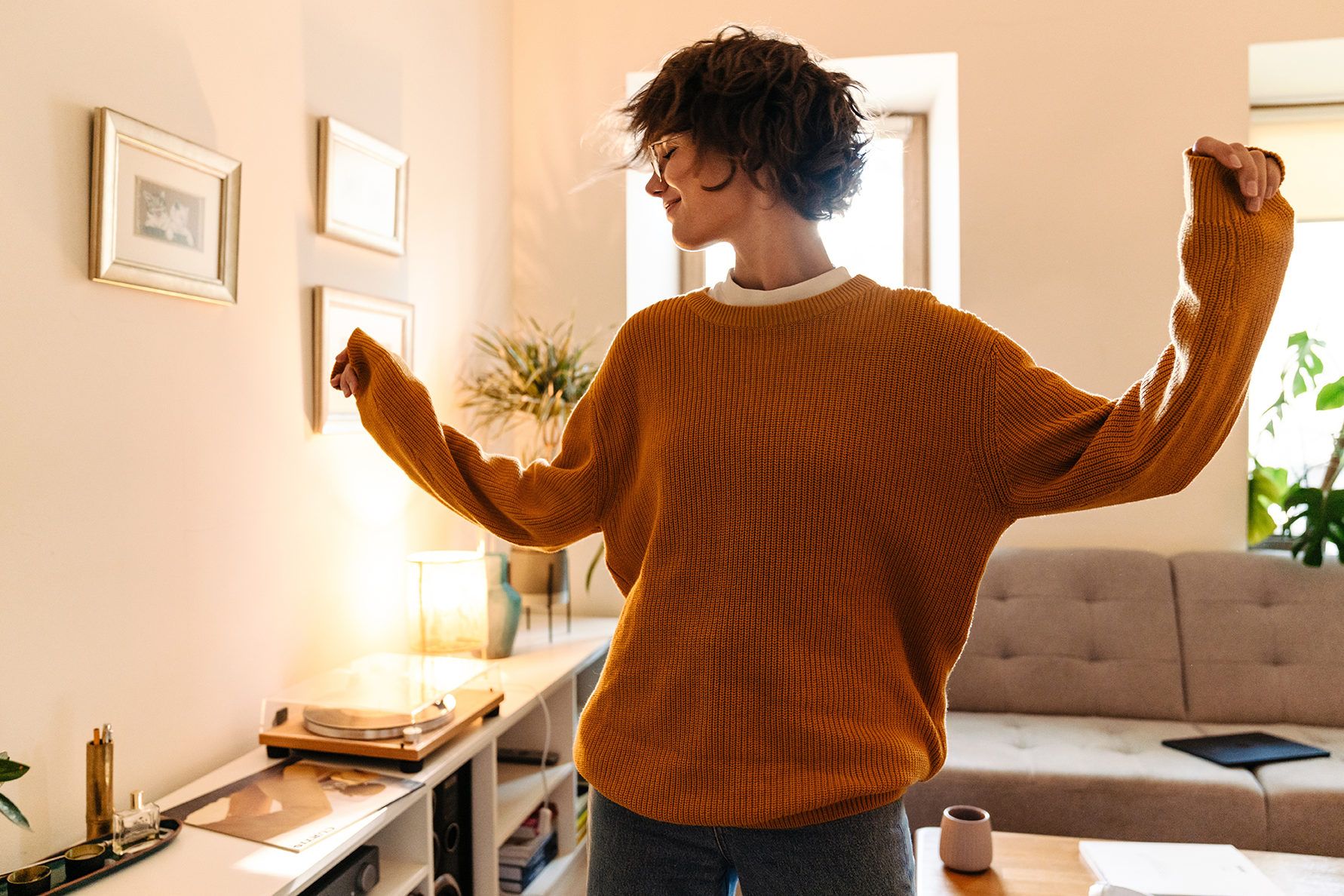 Eine junge Frau tanzt im Wohnzimmer, während sie Musik hört.