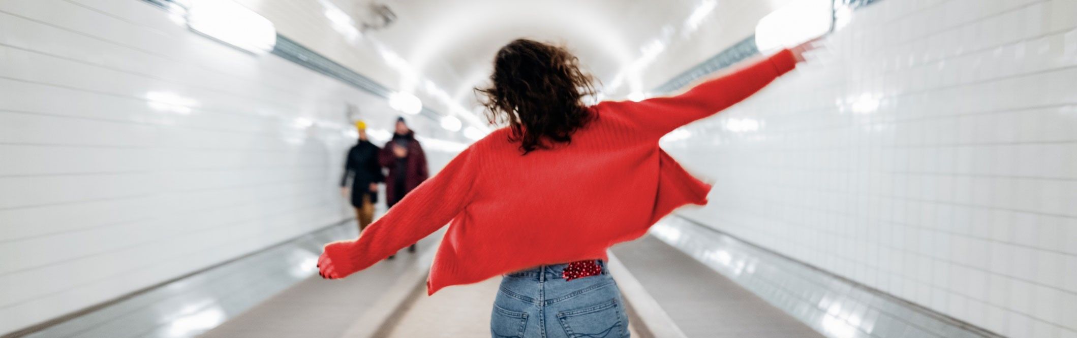 Eine junge Frau läuft fröhlich durch eine U-Bahn-Station.