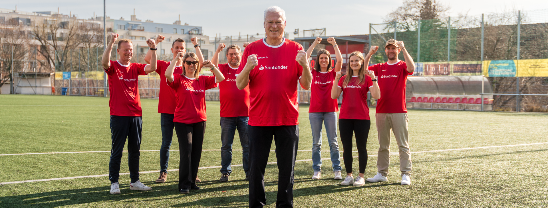 Toni Polster steht vor Santander-Mitarbeitern im roten Fußball-Trikot.