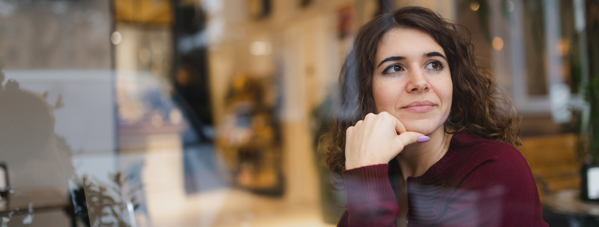 Frau sitzt in Café und blickt gedankenverloren aus dem Fenster.