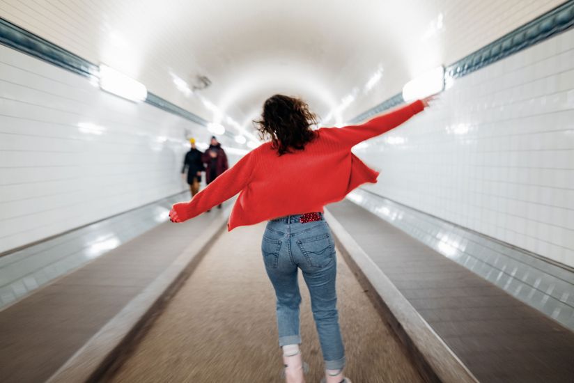 Eine junge Frau läuft fröhlich durch eine U-Bahn-Station.