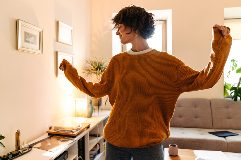 Eine junge Frau tanzt im Wohnzimmer, während sie Musik hört.